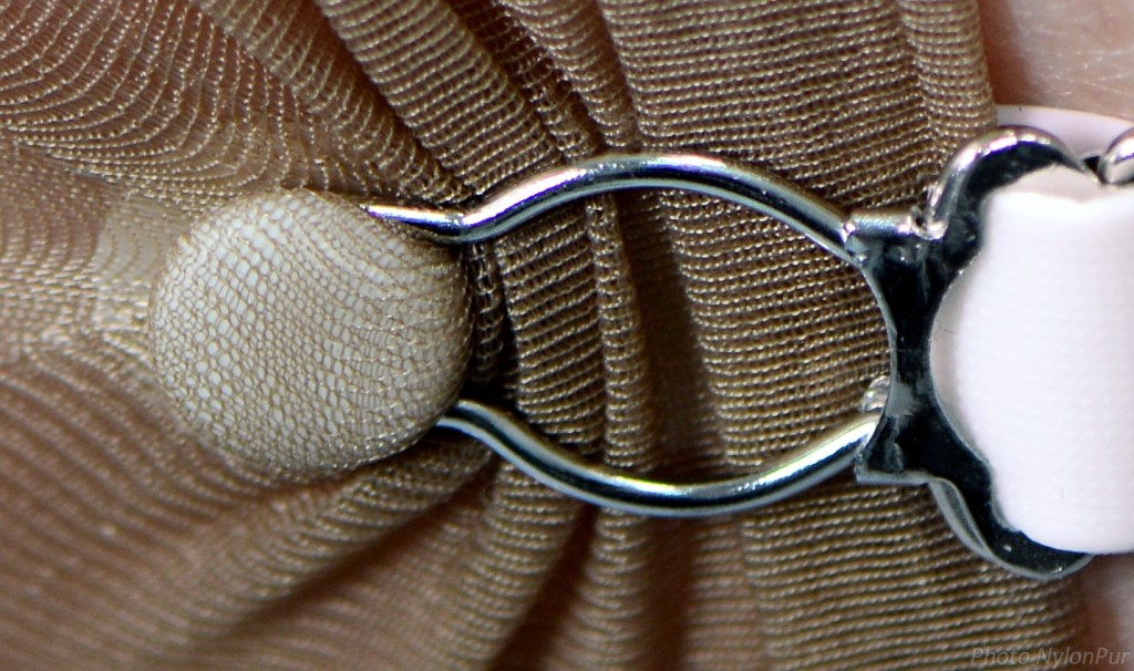 Détail d'une attache de jarretelle, montrant un bouton et un clip en métal sur un bas.