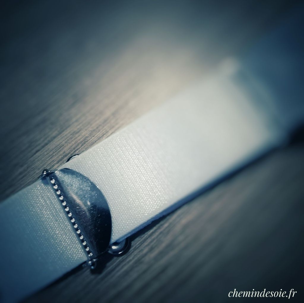 Système de réglage de longueur de jarretelle, avec une pièce métallique qui vient mordre dans l'élastique.