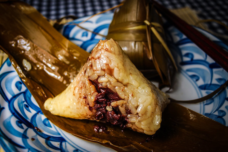 Un zongzi, un triangle de riz gluant farci, présenté sur une assiette décorative avec des feuilles de bambou en arrière-plan.